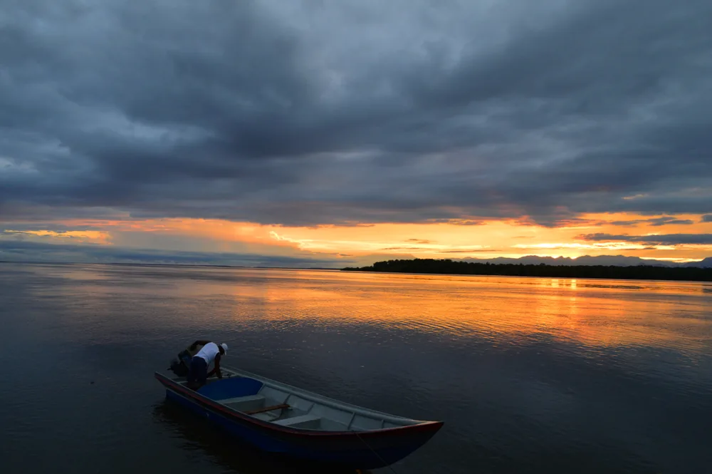 Una persona se inclina sobre una canoa amarrada durante un atardecer dorado sobre el agua