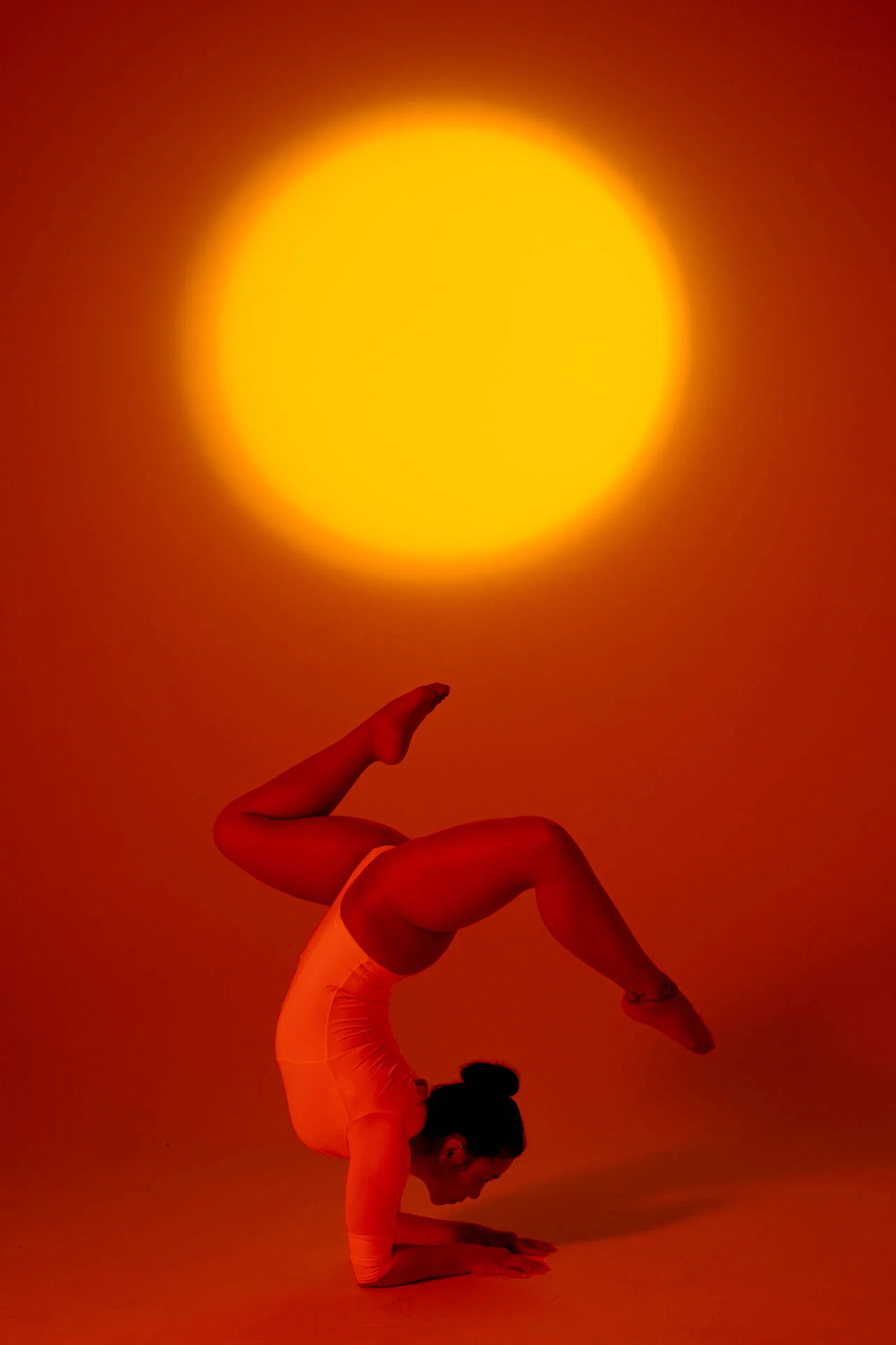 Mujer realizando una parada de manos bajo luz naranja cálida con un sol brillante de fondo
