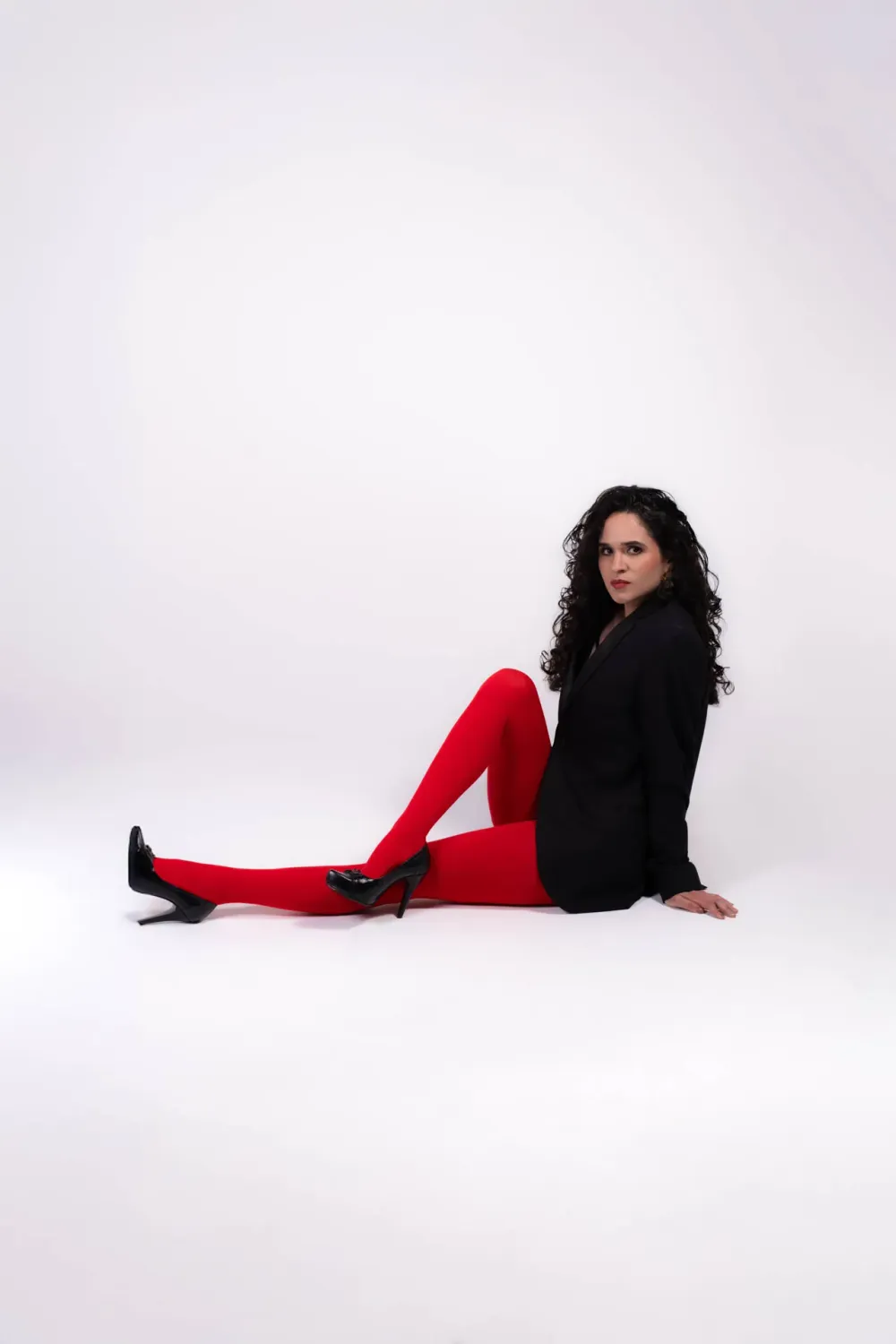 Woman in black blazer and red tights seated on white studio floor